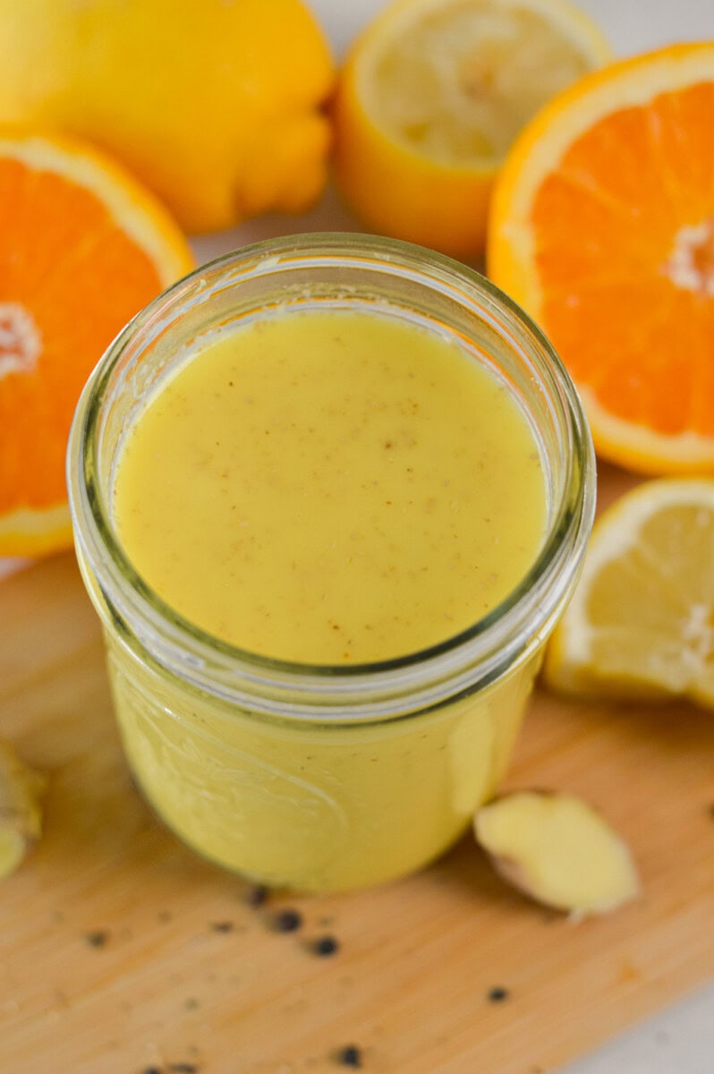Close up of a ginger turmeric shot with oranges in the background.