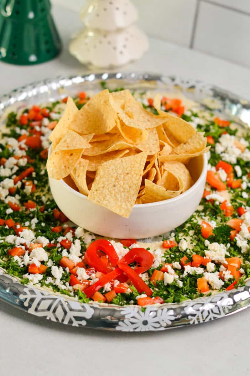 Side angle of hummus wreath with bowl of tortilla chips.