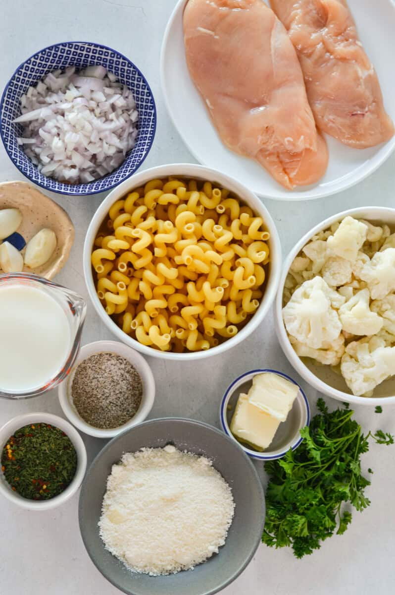 Ingredients including pasta, parmesan, caulilower, parsley, butter, spices, chicken breast, onion, garlic, shallots and milk.