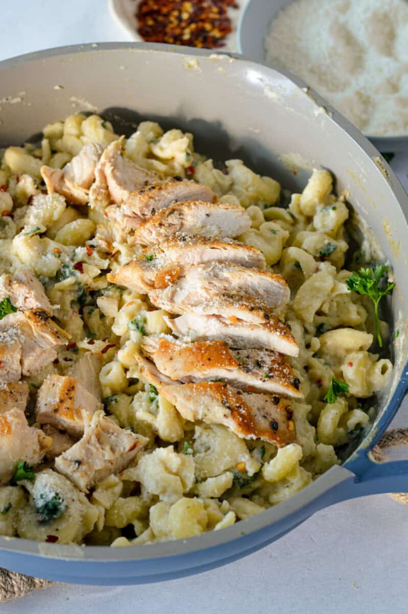Pan of garlic parmesan pasta with sliced chicken breast.