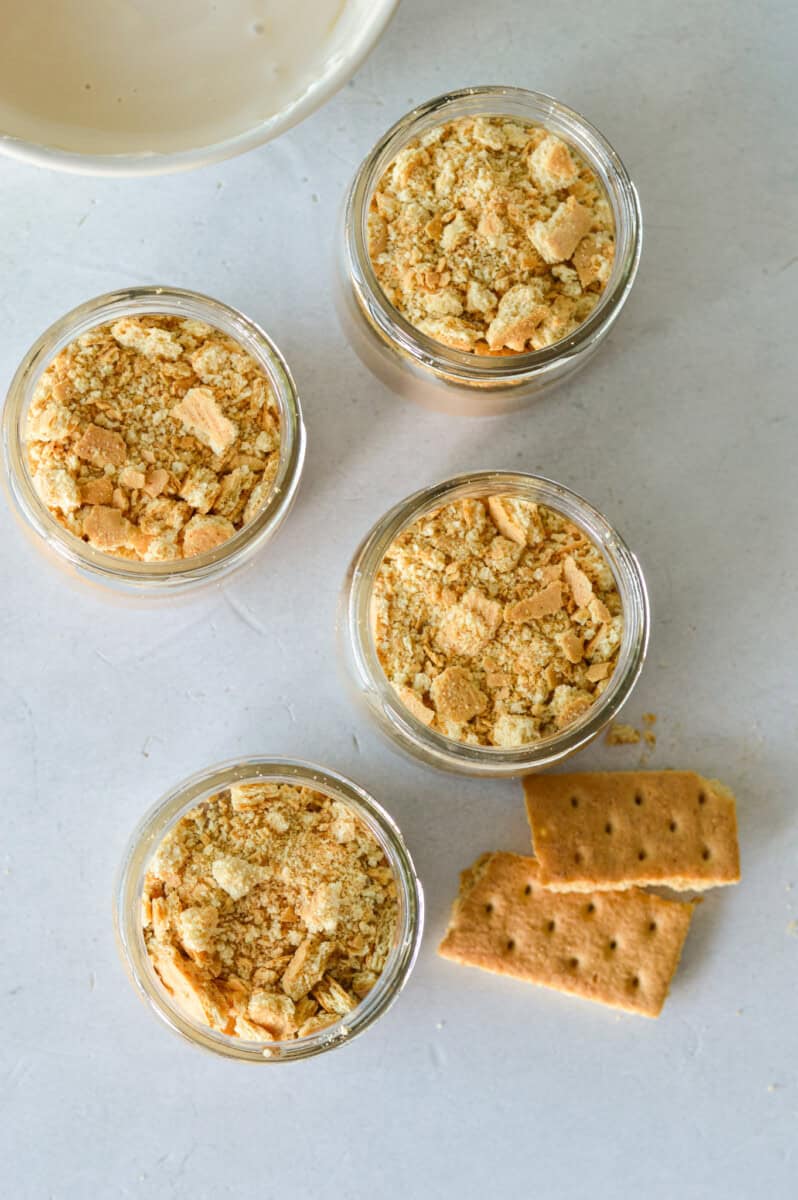 Dividing chia pudding base among 4 jars and topping with crushed graham crackers.
