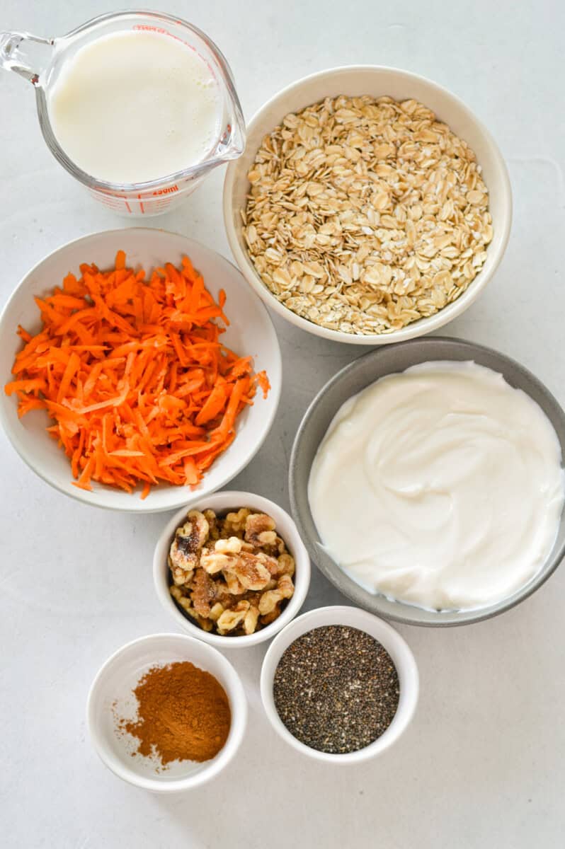 Ingredients including carrots, oats, yogurts, spices, pecans, chia seeds, protein powder and milk.