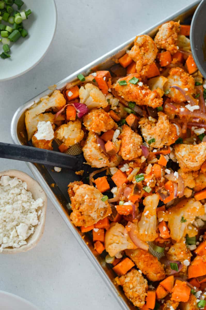 Adding buffalo sauce to sheet pan chicken and potatoes.