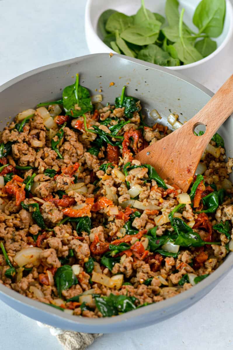 Cooking ground chicken with spinach and sundried tomatoes.
