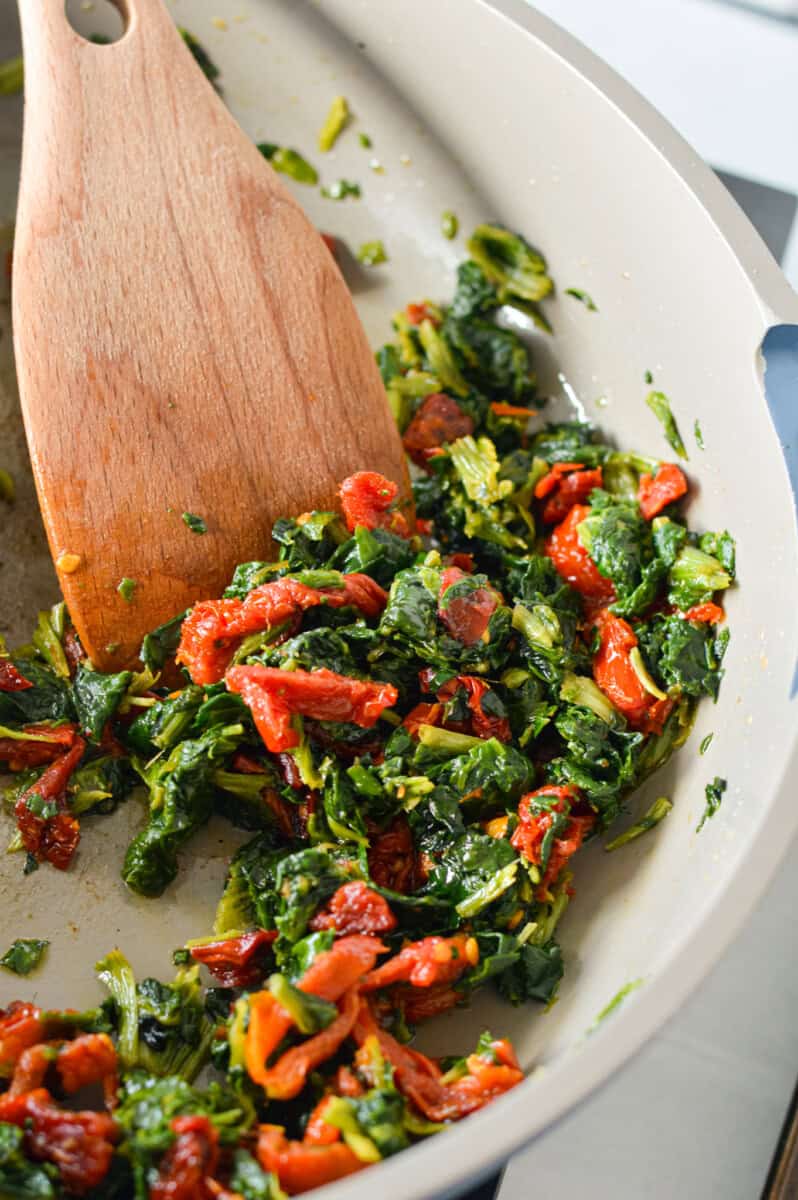 Cooking spinach and sundried tomatoes on a pan.