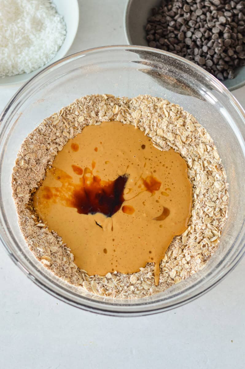 Pouring peanut butter, honey and vanilla into a well in the middle of oats.