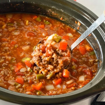 Ladeling a spoonful of stuffed pepper soup from a slow cooker.