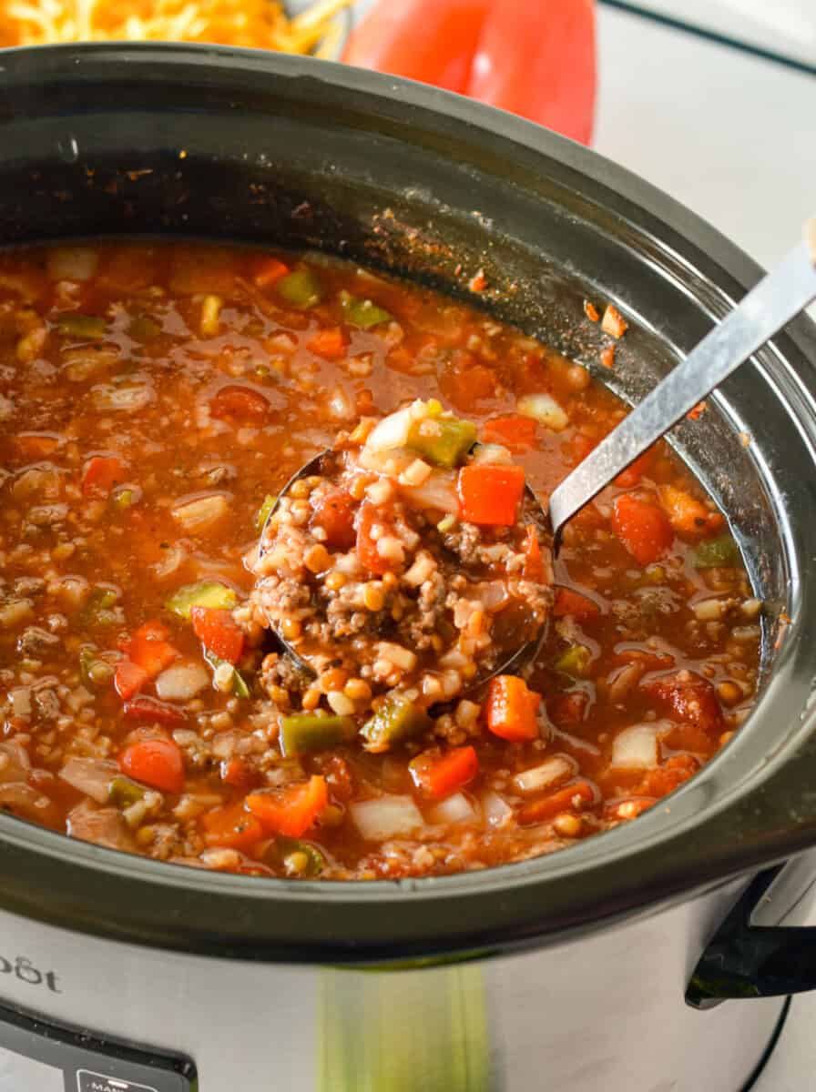 Ladeling a spoonful of stuffed pepper soup from a slow cooker.