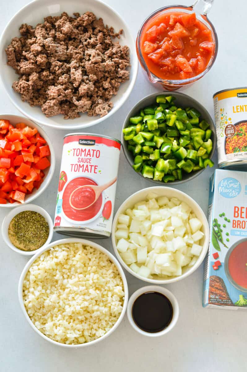Ingredients including ground beef, veggies, tomato sauce, onion, cauliflower rice, spices, shredded cheese, lentils and broth.