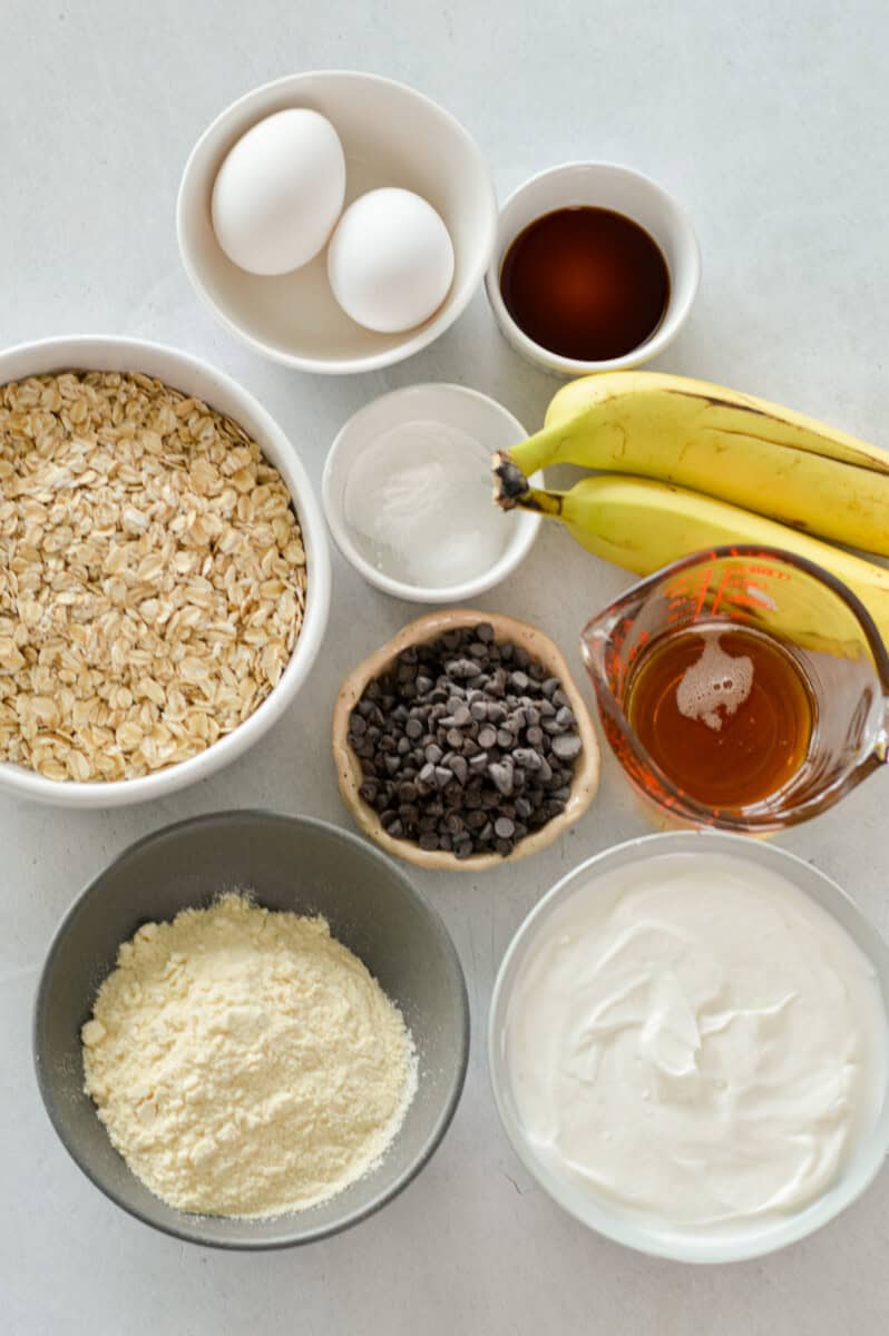 Ingredients including rolled oats, banana,s chocolate chips, protein powder, hrek yogurt, maple syrup and eggs.