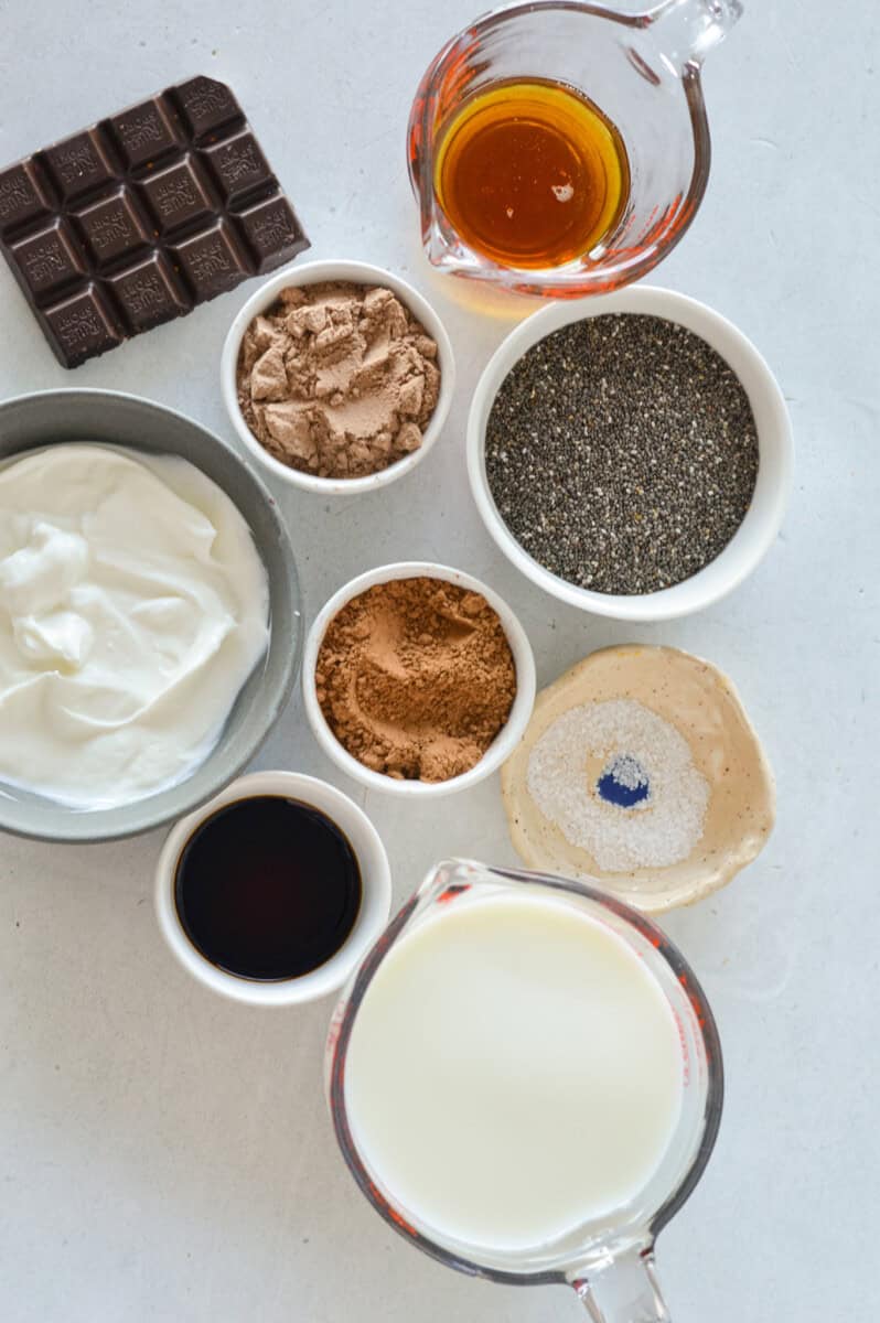 Ingredients including chia seeds, chocolate protein powder, berries, maple syrup, greek yogurt and whipped cream.