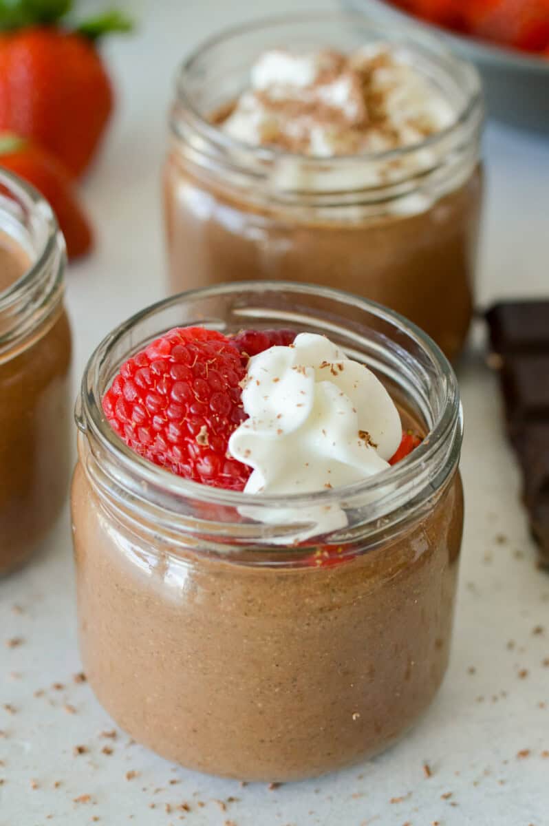 Jar of chocolate chia pudding topped with whipped cream and a strawberry.