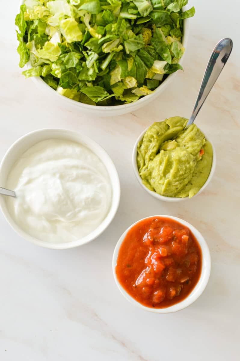 Ingredients including sour cream, salsa, guacamole and shredded lettuce.