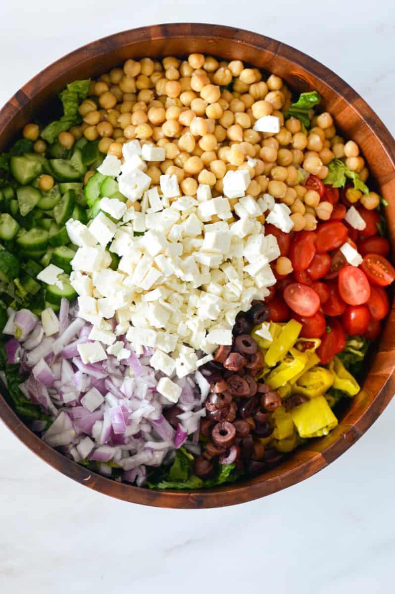 Birds eye view of unmixed chopped salad with feta, olives, red onion, tomato, cucumber and pepperocini.