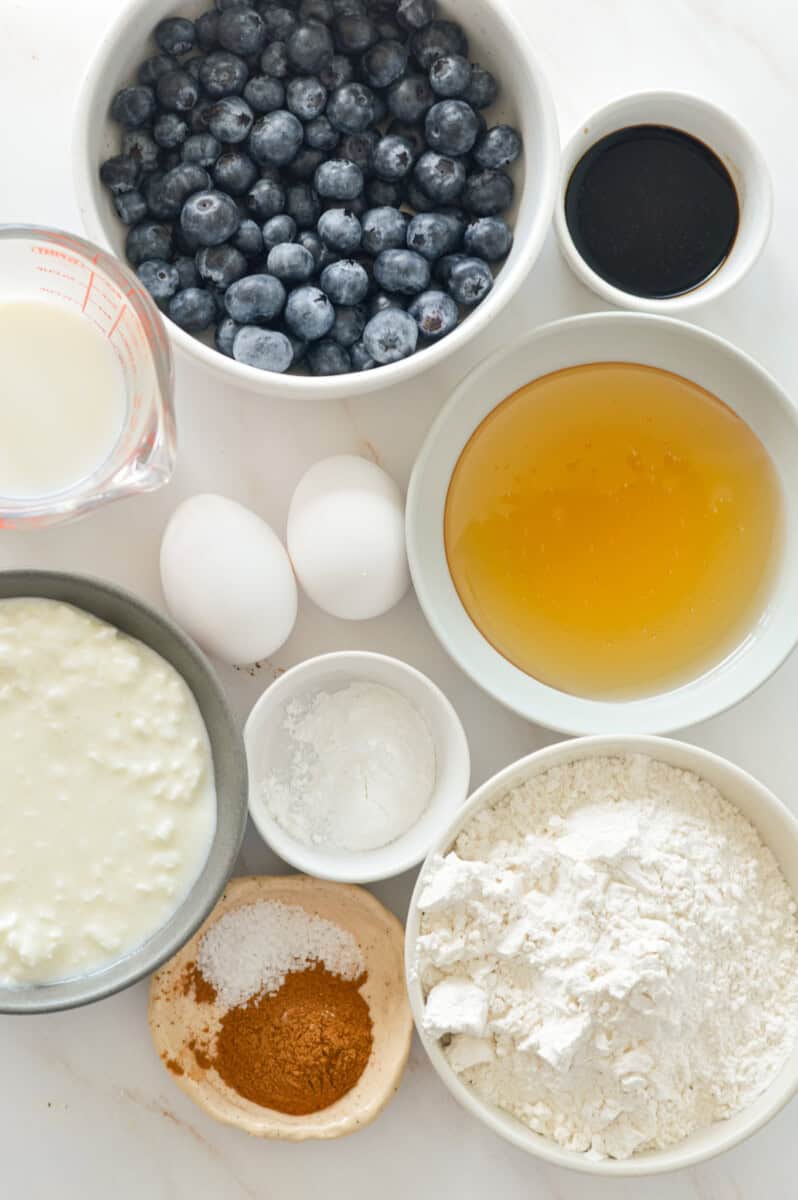 Ingredients including blueberries, olive oil, flour, baking powder, eggs, cottage cheese, vanilla, salt, honey, and milk.