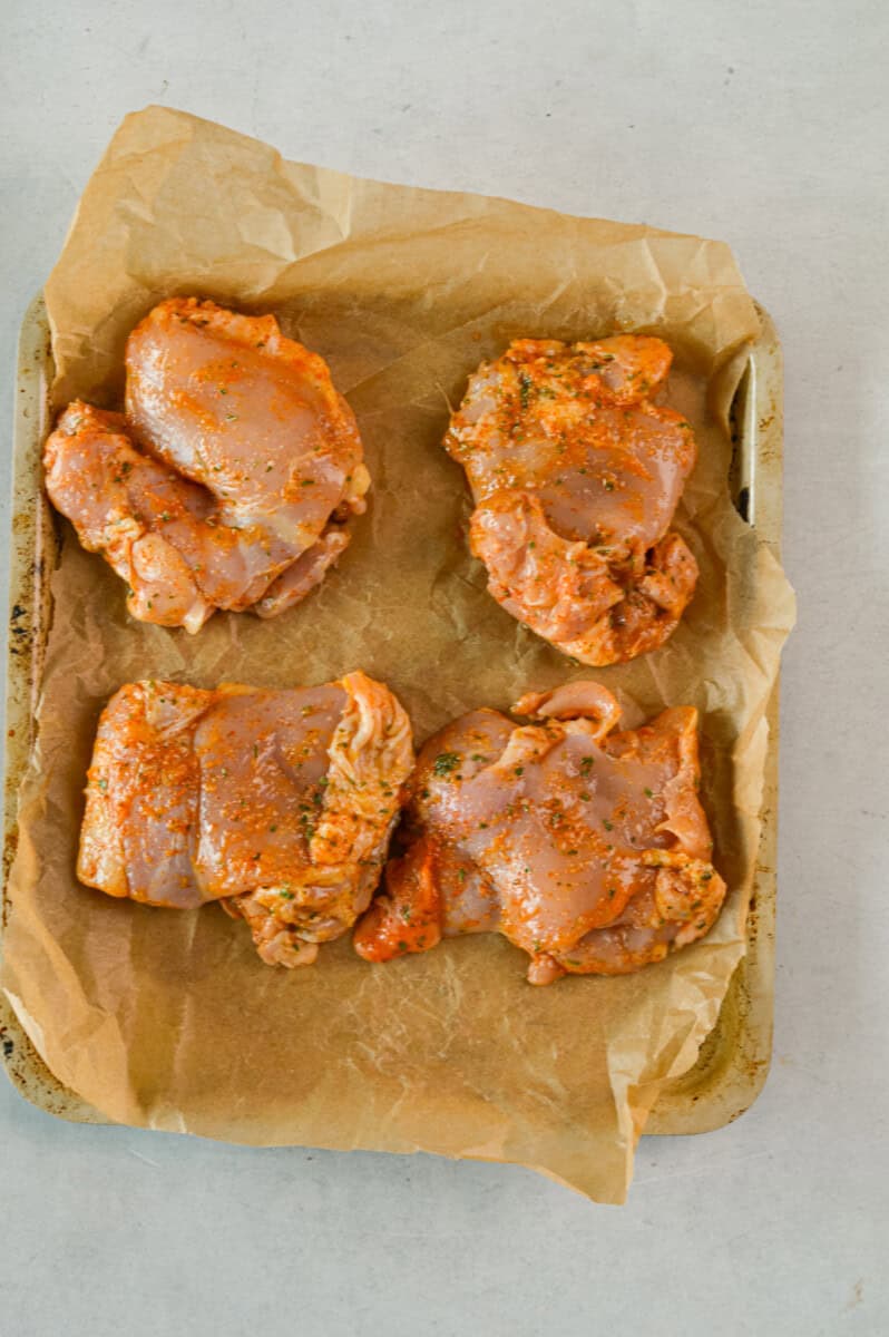 Four raw chicken thighs on an air fryer tray.