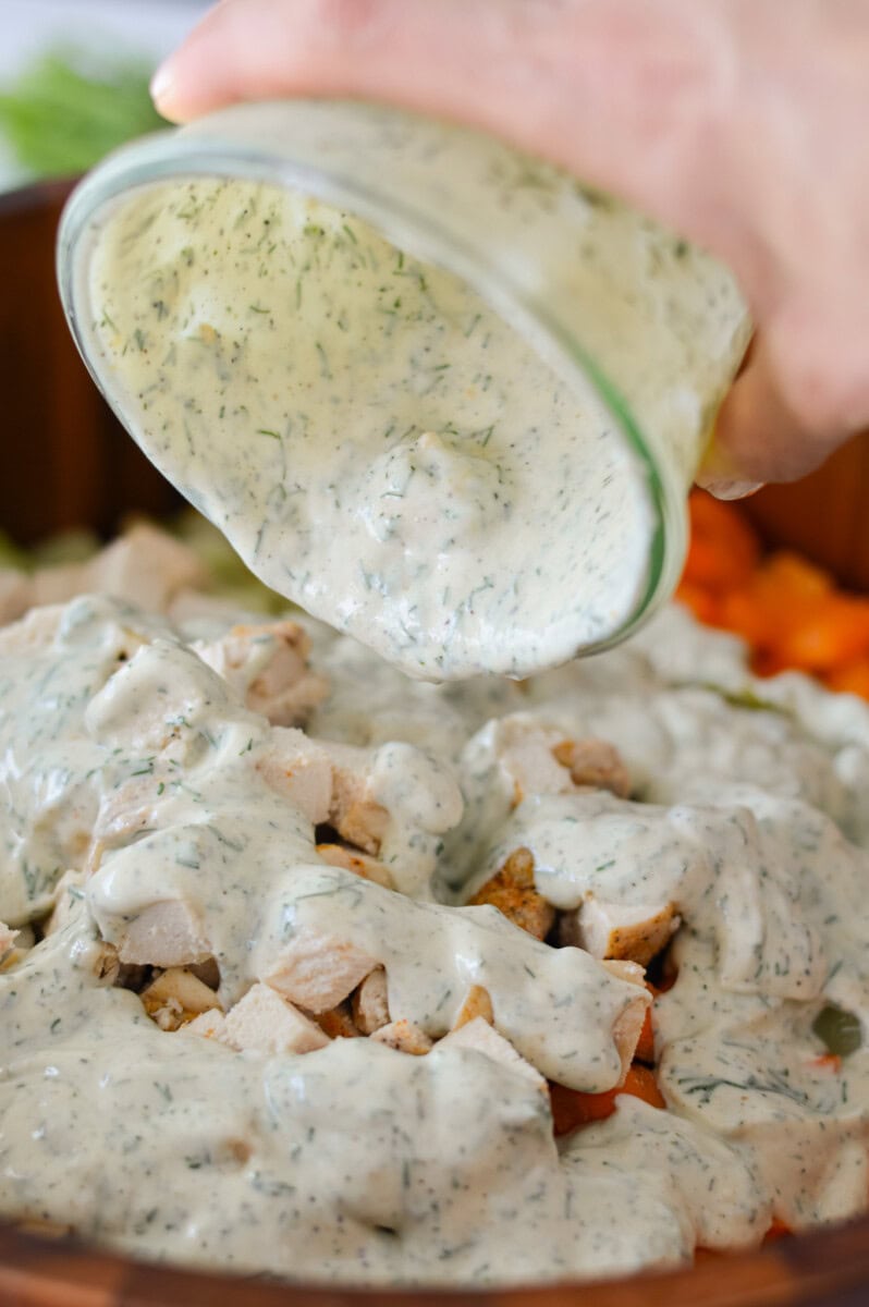 Pouring greek yogurt dressing on chicken macaroni pasta salad.