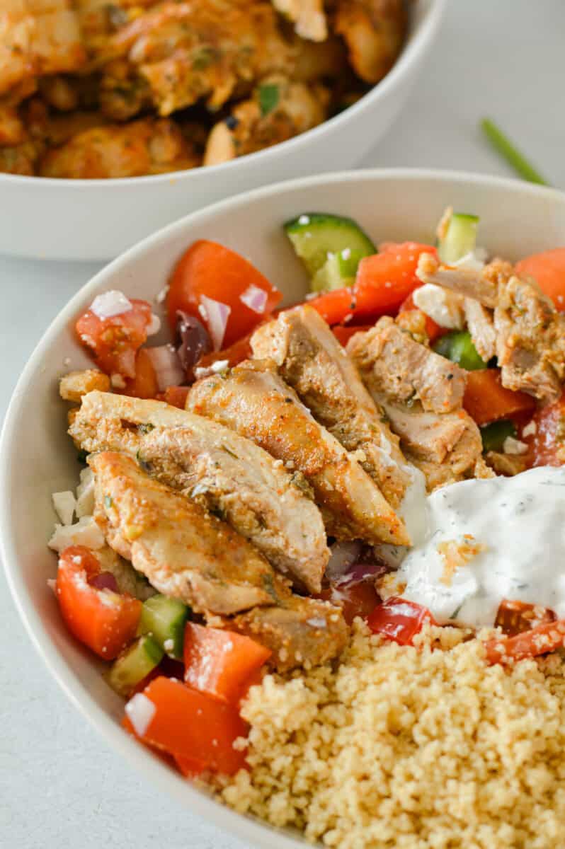 Close up of a dinner bowl with Mediterranean salad, couscous and Greek chicken.