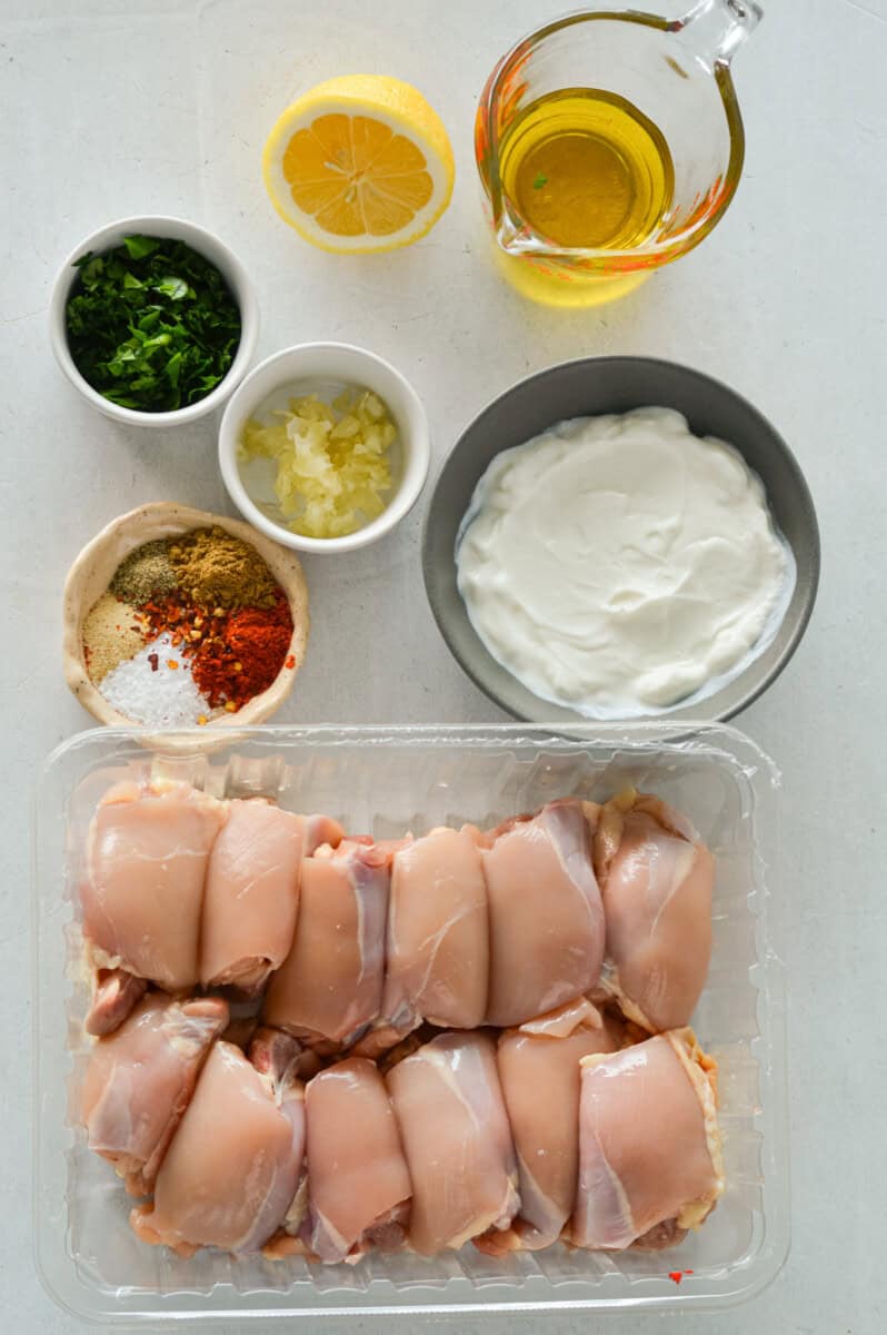 Ingredients including chcicken thighs, greek yogurt, spices, olive oil, lemon juice and parsley.