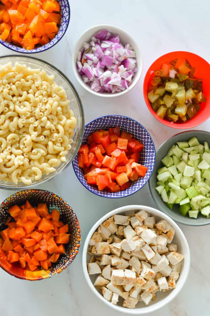 Birds eye of macaroni salad ingredients including macaroni, carrots, chicken, cucumber, bell pepper, red onion and dill pickle.