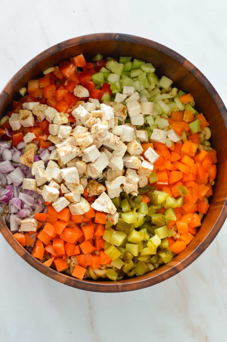 In a large bowl combine the cooked pasta,diced celery, bell peppers, carrots, red onions, pickles and cooked chicken. 