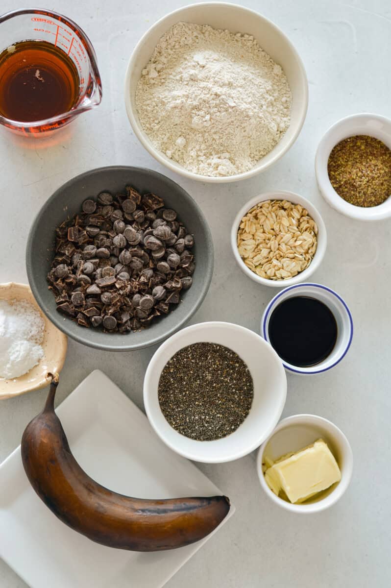 Ingredients including banana, chocolate chips, oat flour, oats, chia seed, flaxseed, maple syrup, butter and flakey sea salt.