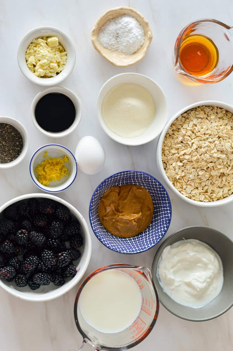 Ingredients including oats, oat flour, yogurt, blackberry, lemon zest, chia seeds, milk, collagen, peanut butter and an egg.