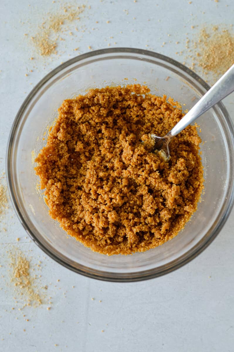Mixing graham crumbs with butter to form cheesecake crust.