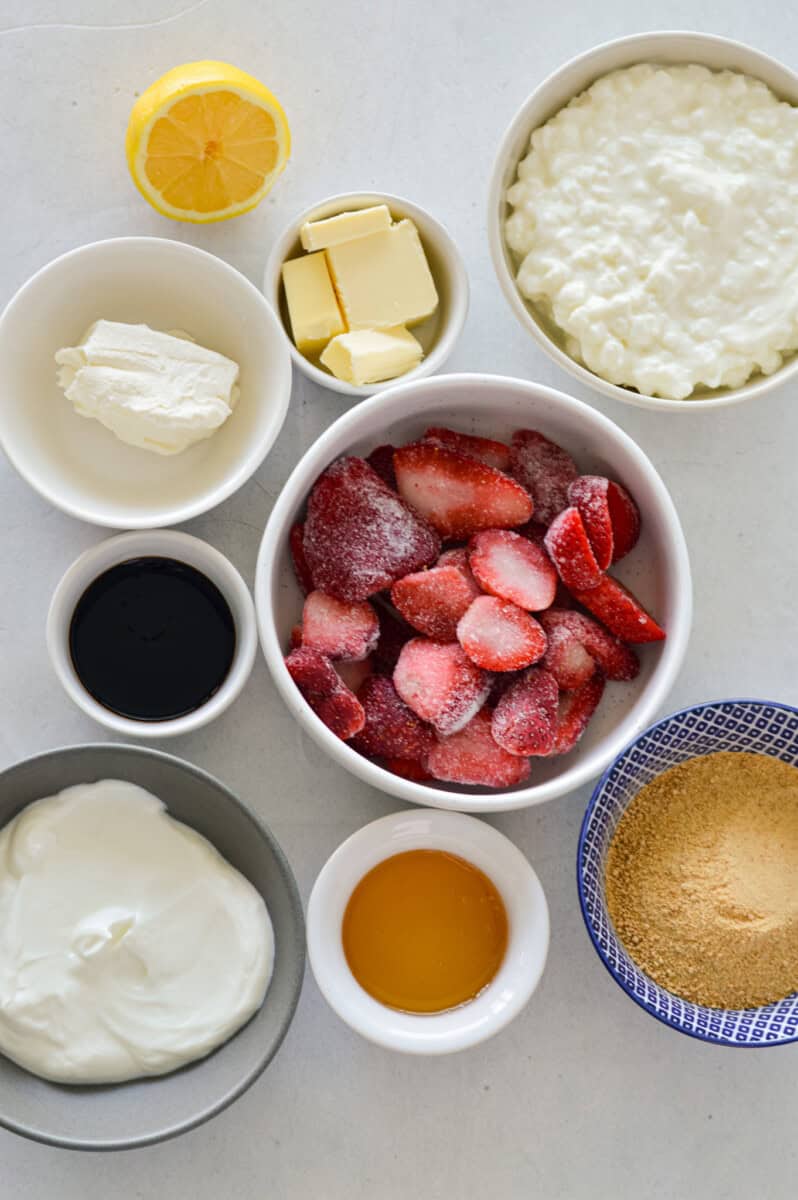Birds eye of ingredients including graham crackers, butter, greek yogurt, cottage cheese, lemon zest, strawberries, vanilla and honey.