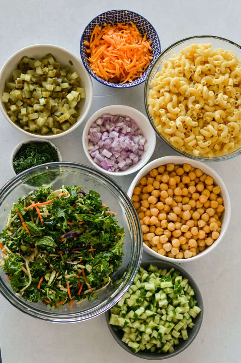 Birds eye of ingredients including chickpeas, kale, red onion, pasta, dill pickle, fresh herbs and carrots.