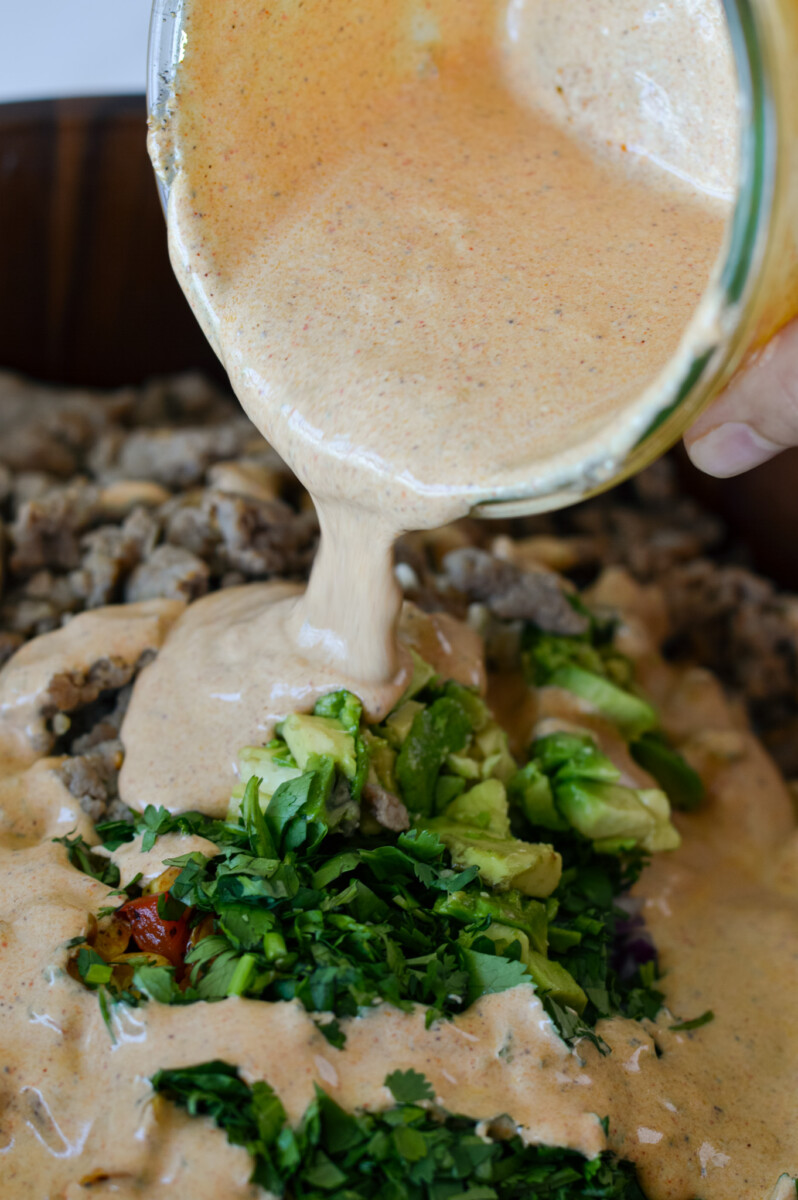 Adding salad dressing to elotes pasta salad.