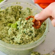 Close up of hand dipping a pretzel into bowl of kale edamame dip.