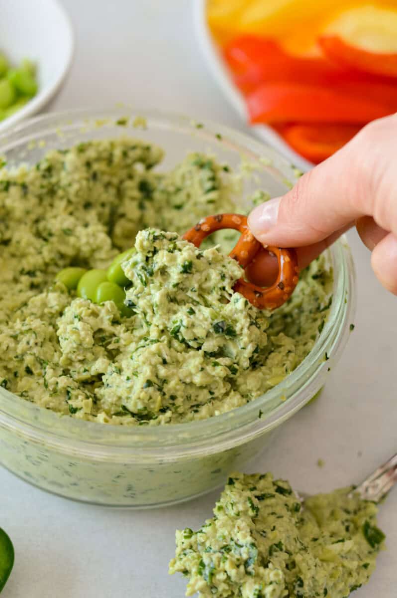 Close up of hand dipping a pretzel into bowl of kale edamame dip.