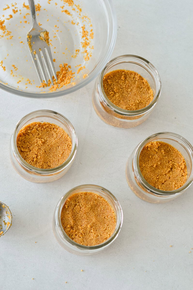 Adding cheesecake crust to bottom of glass jars.
