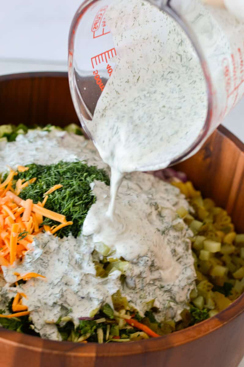 Pouring salad dressing on dill pickle pasta salad.