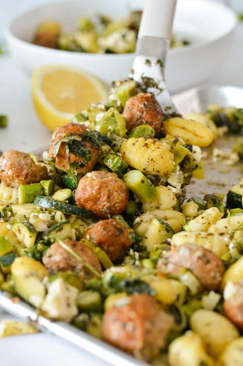Close up of gnocchi, sausage and asparagus on a baking tray.
