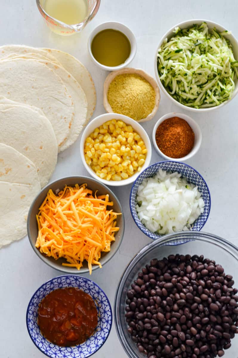 Ingredients including shredded cheese, onion, corn, spices, black beans, salsa, nutritional yeast, tortilla and zucchini.
