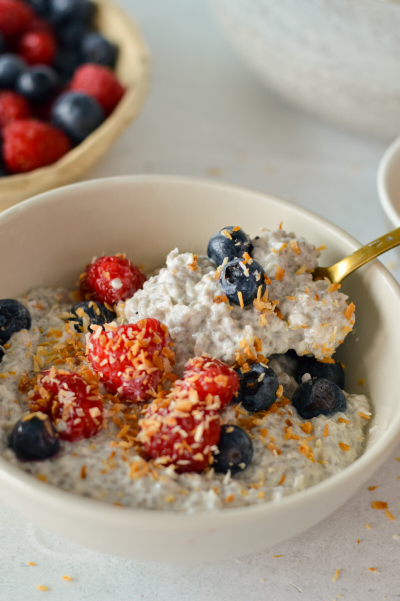Close up of a spoon in a bowl of coconut chia pudding topped with berries.