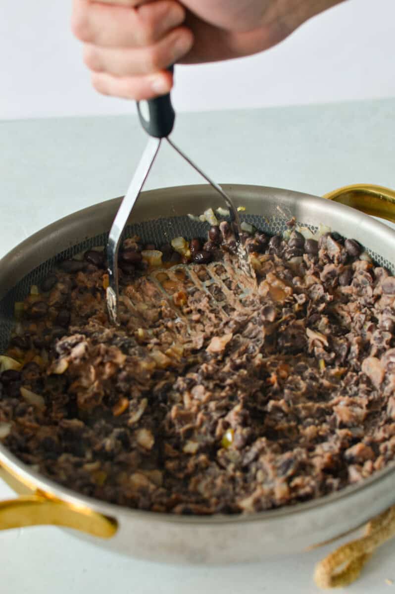 Mashing black beans in a pan.