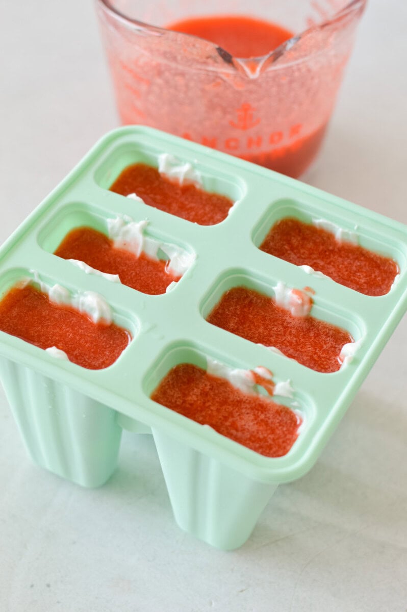 Pouring blended strawberries into a popsicle mold.