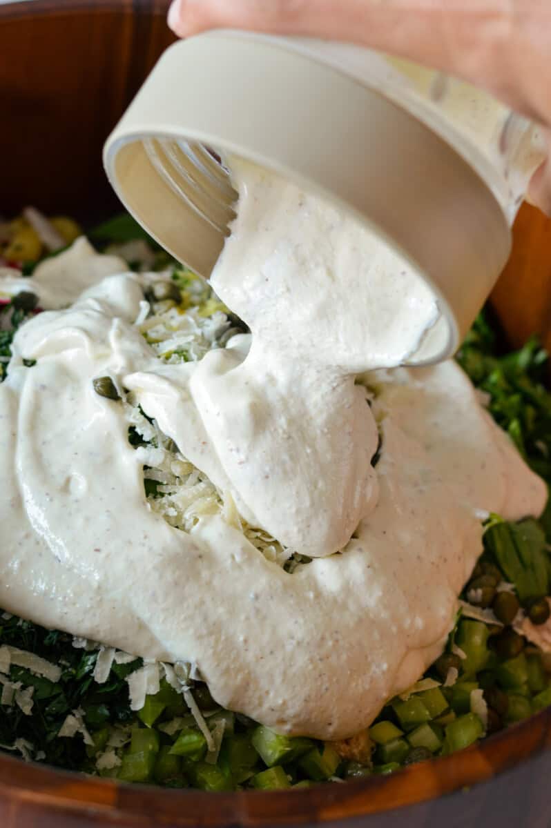 Pouring creamy dressing into tuna pasta salad.