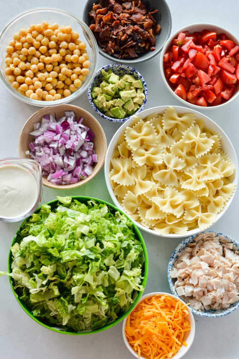Ingredients including bowtie pasta, bacon, chickpeas, avocado, cheese, chicken, lettuce and greek yogurt dressing.