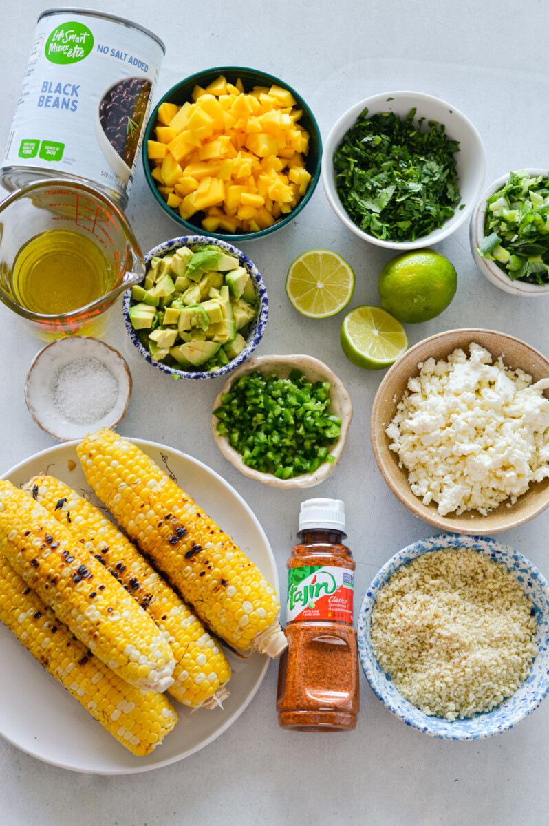 Ingredients including corn, black beans, mango, jalapeno, feta cheese, avocado, cilantro, green onion, salt, olive oil, panko, tajin, and lime.