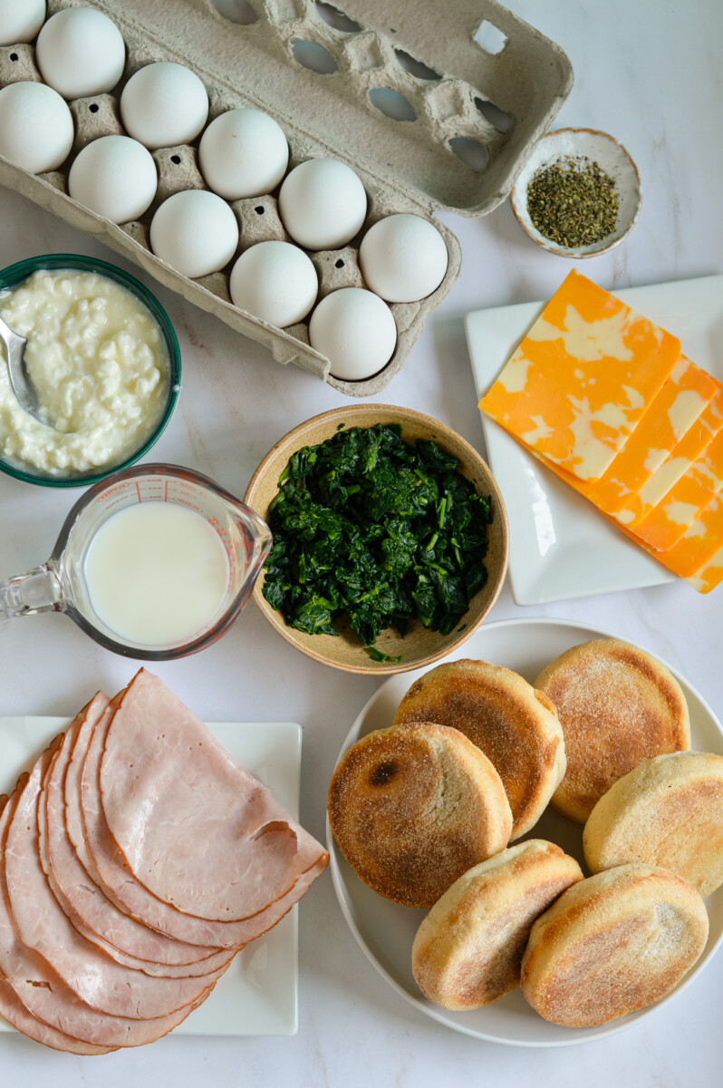 Ingredients including eggs, cheese, spinach, milk, cottage cheese, meat and english muffins.