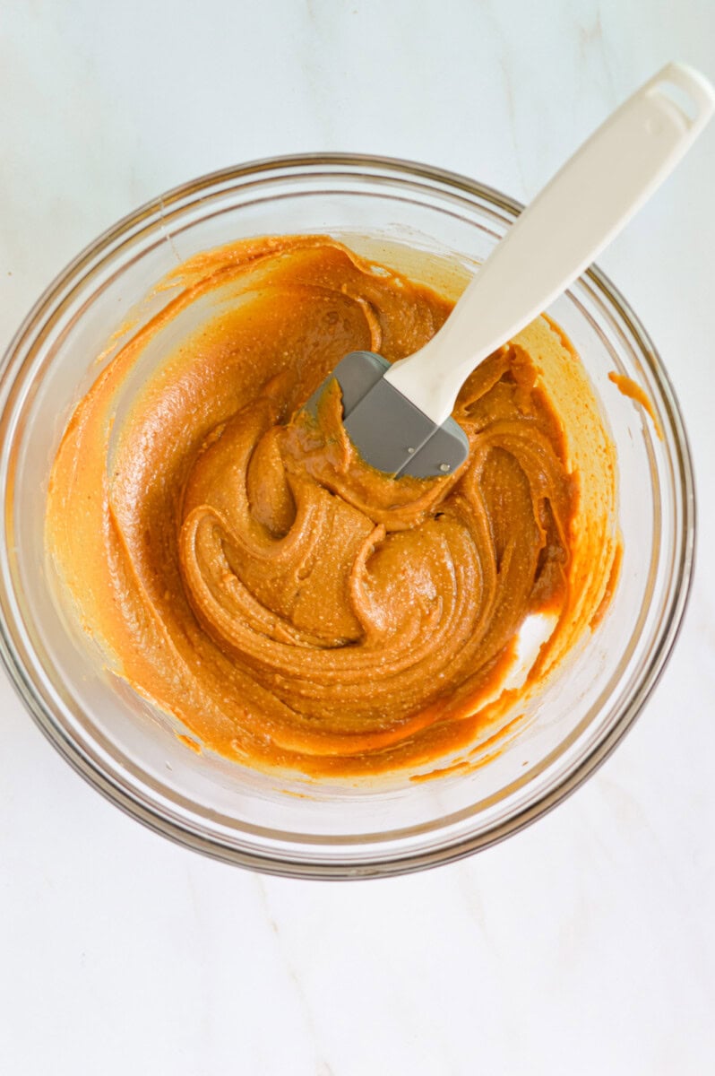 Mixing peanut butter in a bowl with wet ingredients.