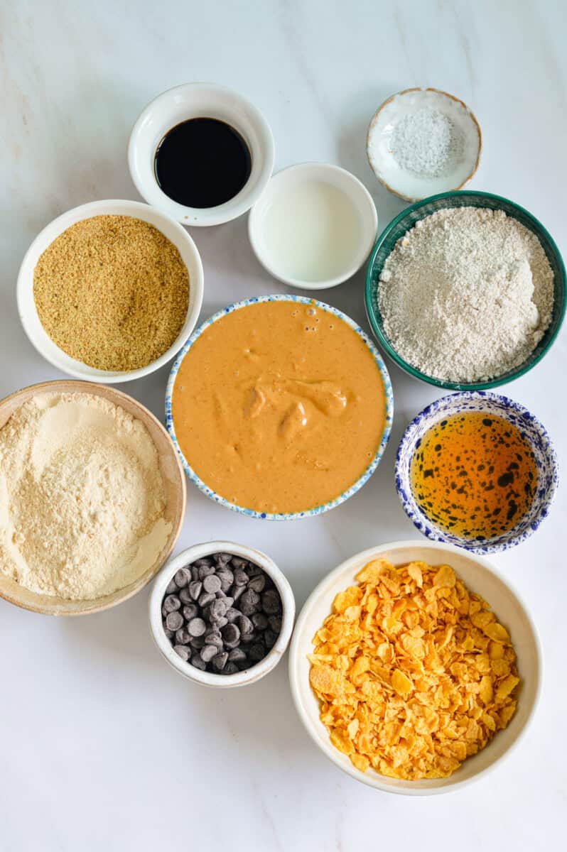 Ingredients including peanut butter, oat flour, protein powder, cornflakes, chocolate chips, maple syrup, honey and milk.