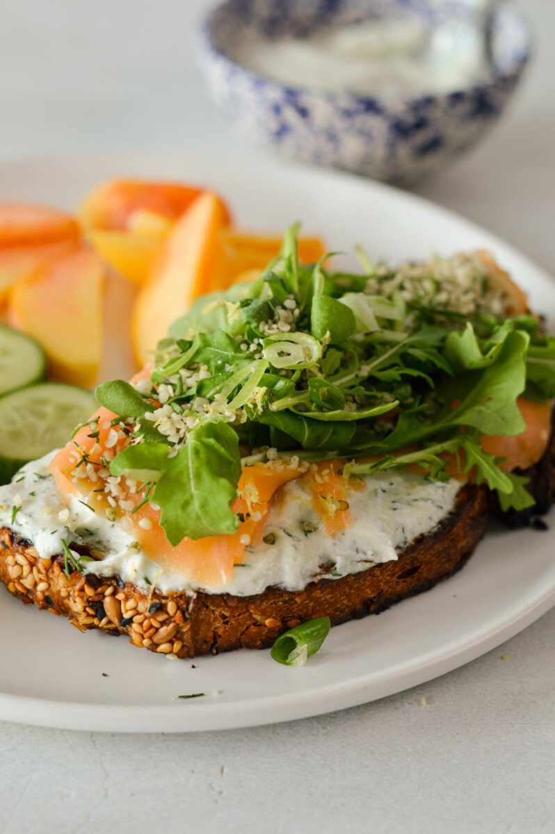 Slice of toast with whipped ricotta cheese, smoked salmon and arugula.